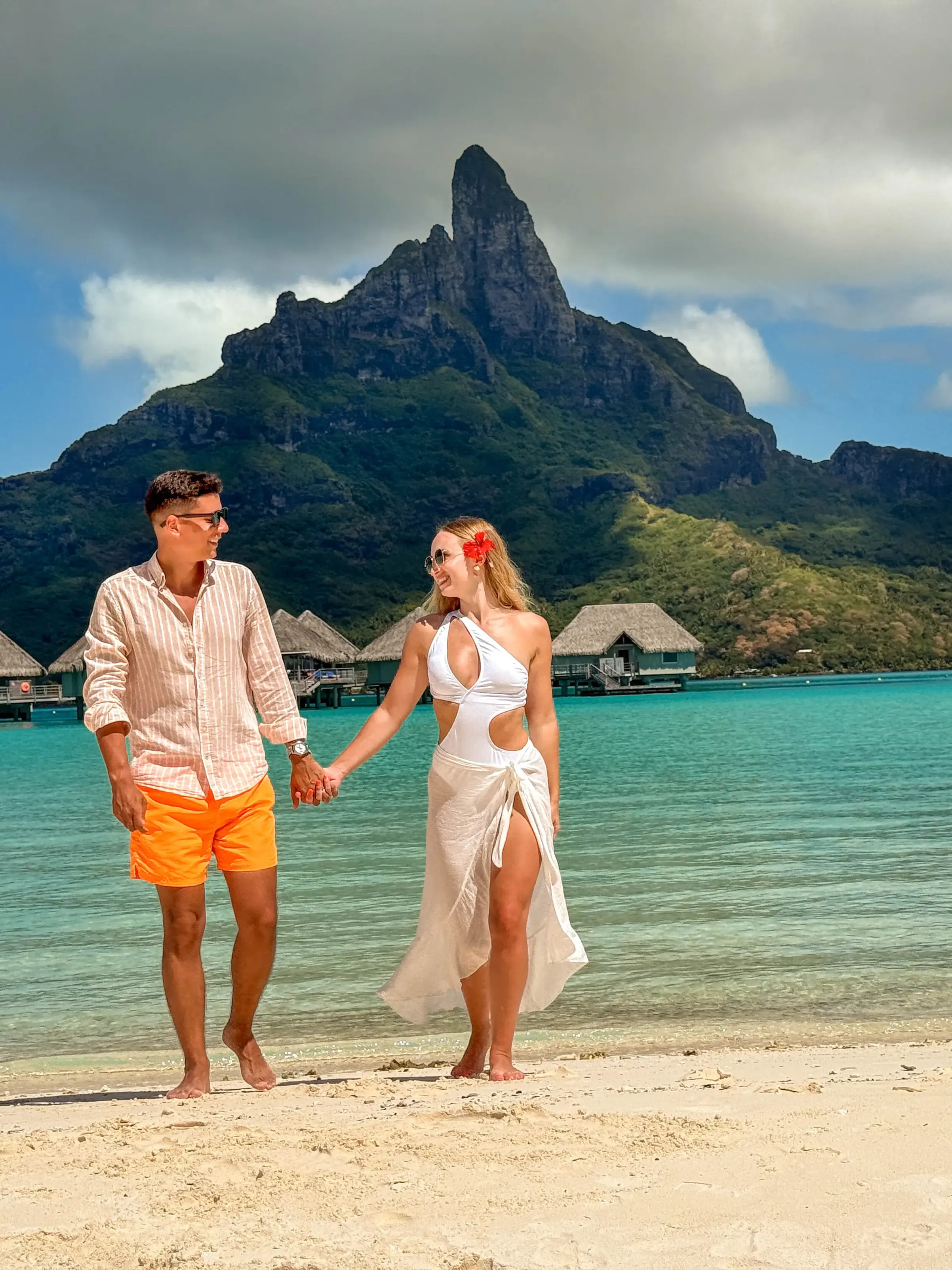 Andrei and Cristina walking hand in hand on a beach with Mount Otemanu in the background